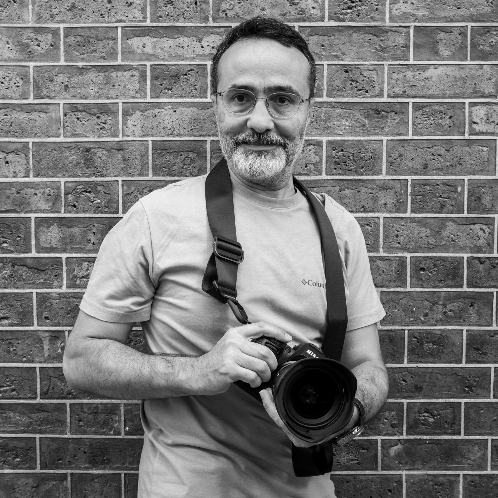 Tuğla duvar önünde fotoğraf makinesiyle gözlüklü adam